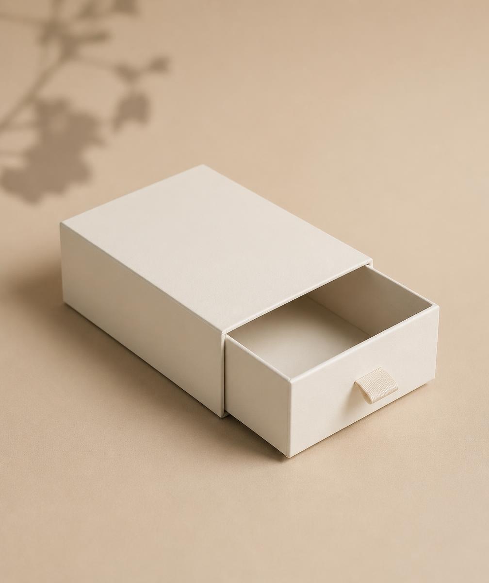 Matte off-white rigid drawer box slightly open on a warm beige backdrop